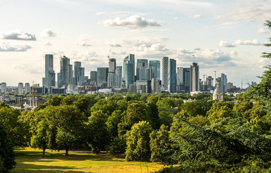 A panoramic view of a lush, well-maintained garden with a neatly trimmed lawn and a variety of green trees and shrubs in the foreground. The garden features a paved pathway winding through the space,